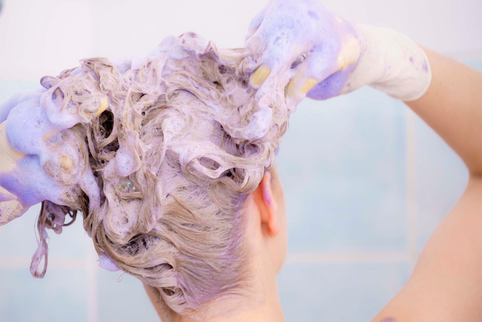 mujer aplicando shampoo azul en cabello mojado